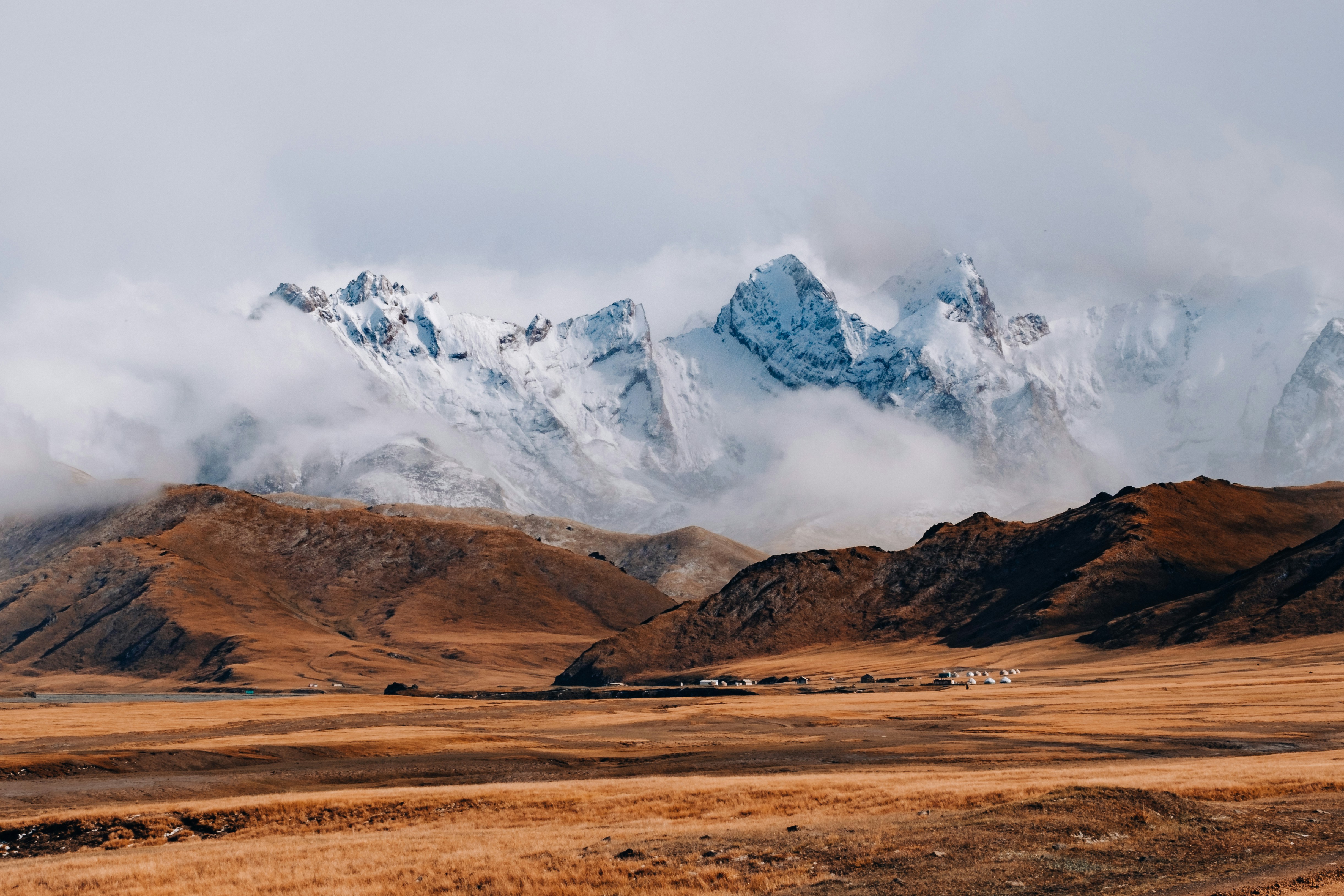 Snow-capped Tien Shan mountains rising over open steppe and yurt camps in Kyrgyzstan